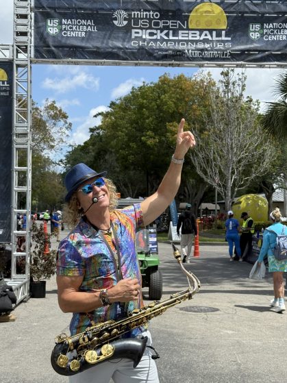 Saxophonist in a colorful patterned shirt and blue fedora performing outdoors at a private event held at the US Open Pickleball Championships
