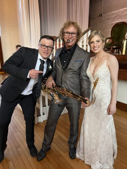 MattyB Entertainment saxophonist posing with bride and groom holding saxophone at wedding reception