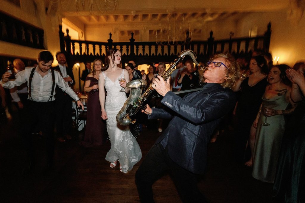 MattyB playing saxophone as the bride dances on the wedding reception dance floor surrounded by cheering guests