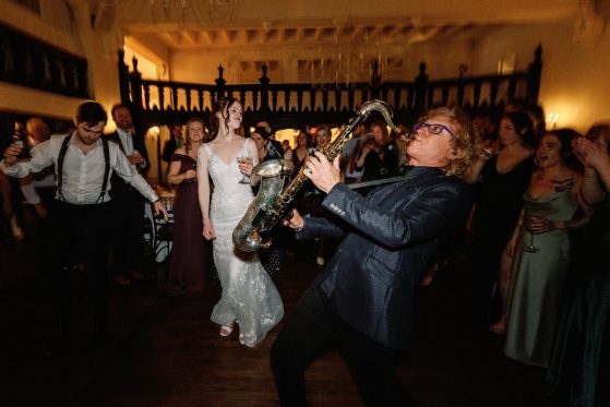 MattyB playing saxophone as the bride dances on the wedding reception dance floor surrounded by cheering guests