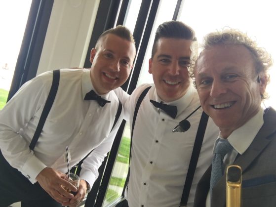 MattyB taking a selfie with groomsmen wearing suspenders and bow ties at a bright wedding reception