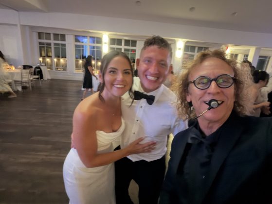 MattyB wearing a headset microphone poses with the bride and groom on the wedding reception dance floor